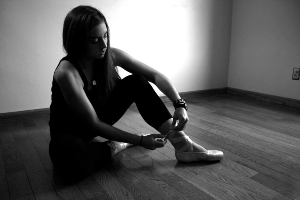 girl sitting on hardwood floor tying pointe shoe